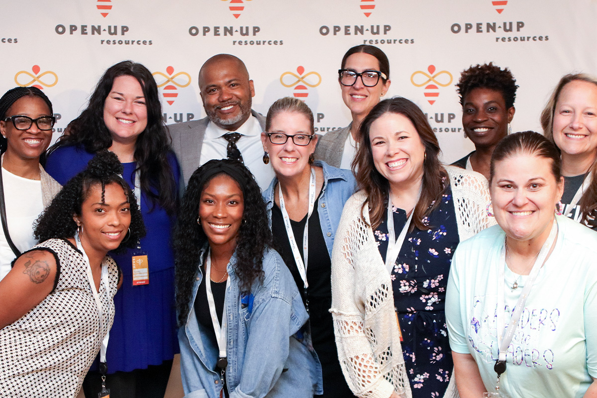 A diverse group of smiling people posing for a photo at HIVE with 'open-up resources' banners in the background.